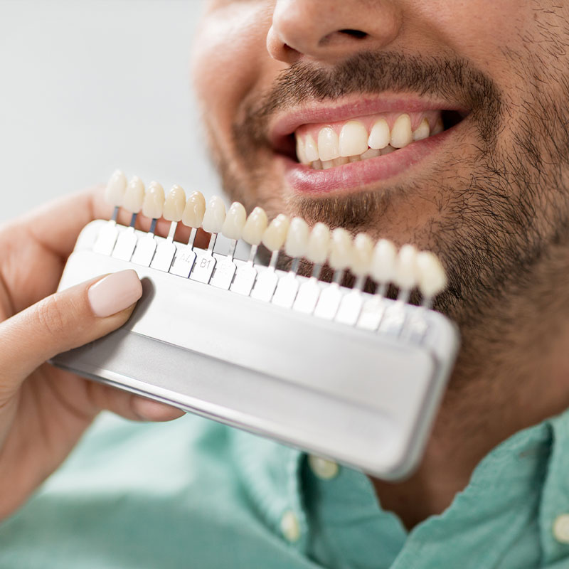 The image depicts a man smiling while holding an electric toothbrush with multiple bristles.