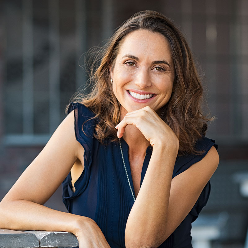 Woman in blue top leaning on railing, smiling.